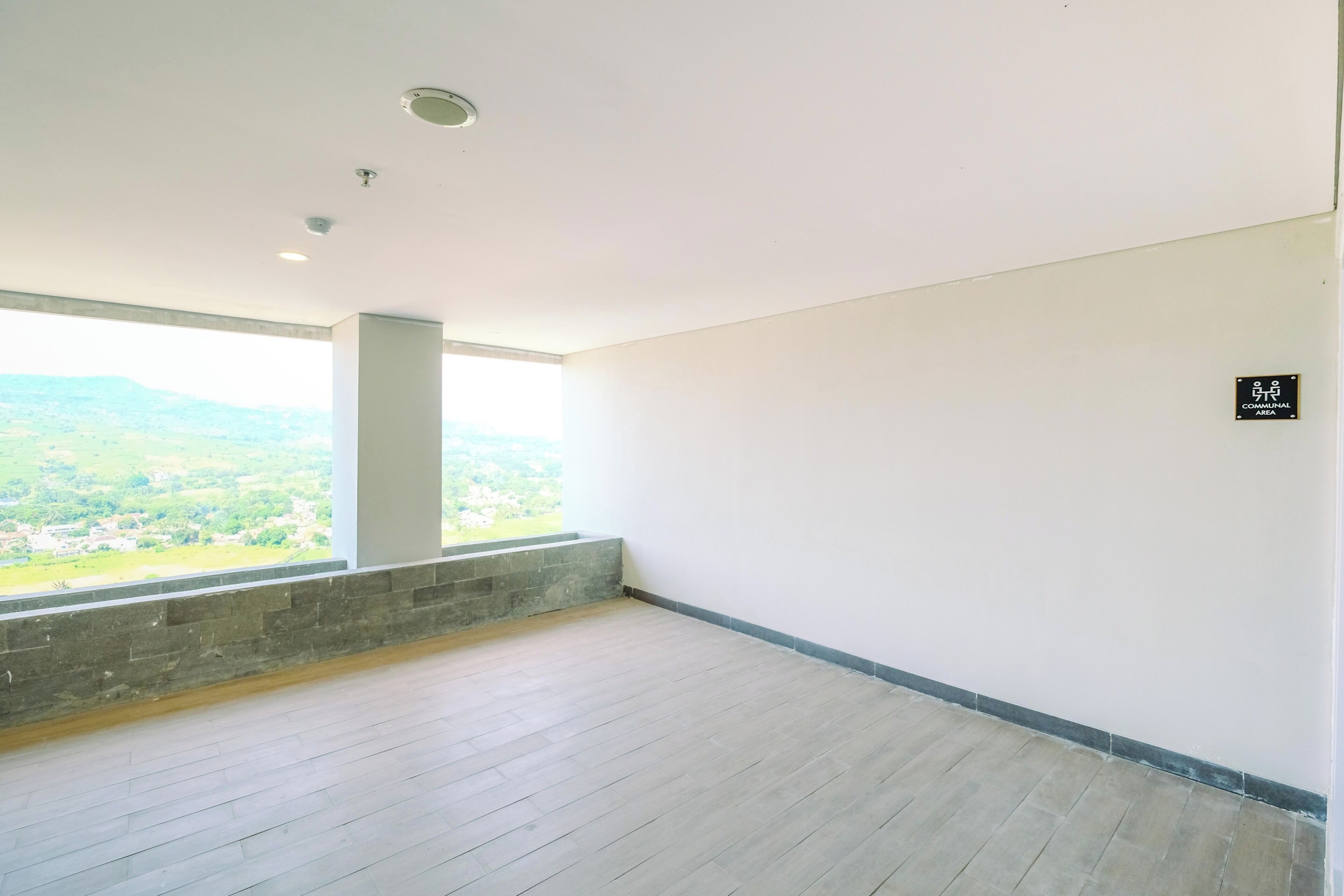 A spacious room with a large window offering a view of a green landscape.