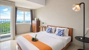 A hotel room with a bed, a bedside table, a lamp, a view of greenery outside, and a window with curtains. - Peaceful Studio No Kitchen At Apartment Lrt City Sentul - Royal Sentul Park (Bogor)