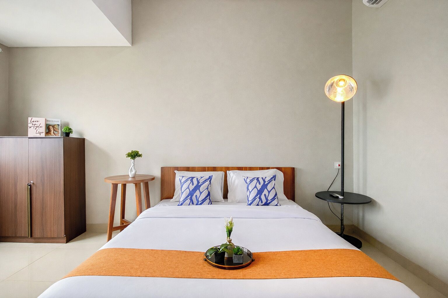 A hotel room with a bed, a bedside table, a lamp, a wardrobe, and a small plant.