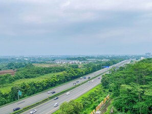 A highway with multiple lanes, surrounded by dense greenery and distant buildings. - Peaceful Studio No Kitchen At Apartment Lrt City Sentul - Royal Sentul Park (Bogor)
