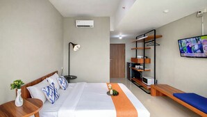 A hotel room with a bed, bedside table, lamp, TV, and a shelf with items. - Peaceful Studio No Kitchen At Apartment Lrt City Sentul - Royal Sentul Park (Bogor)