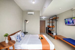 Una habitación de hotel con cama, mesita de noche, lámpara, televisor y una estantería con objetos.