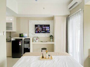 Ein Hotelzimmer mit einem Bett, einem an der Wand befestigten Fernseher, einer kleinen Küchenzeile und einem Fenster mit Vorhängen.