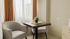 A room with a sofa, a small table with a plant, a chair, and a cabinet. - Tranquil Studio For 2 Pax At Royal Sentul Park Apartment (Bogor)