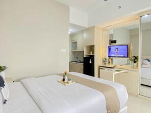 Quarto de hotel com cama, escrivaninha, televisão e cozinha compacta.