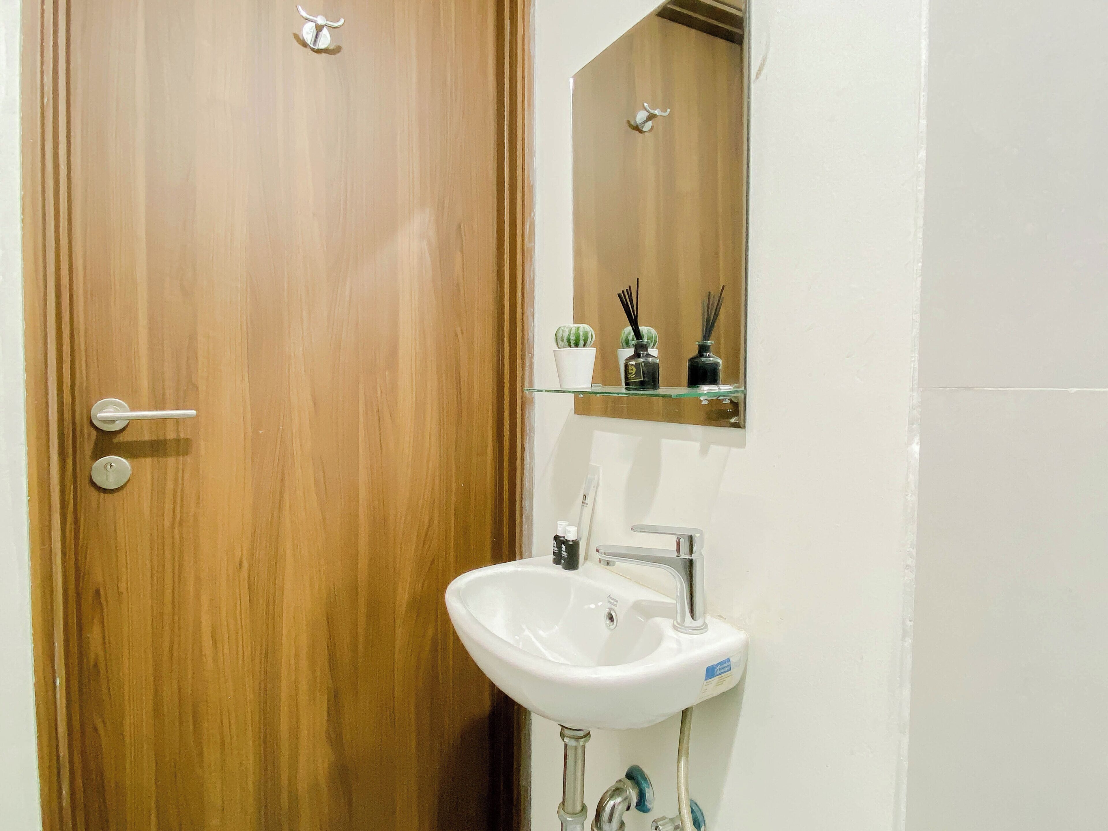 Une porte en bois avec une poignée argentée, un lavabo blanc avec un robinet chromé et un miroir au-dessus.