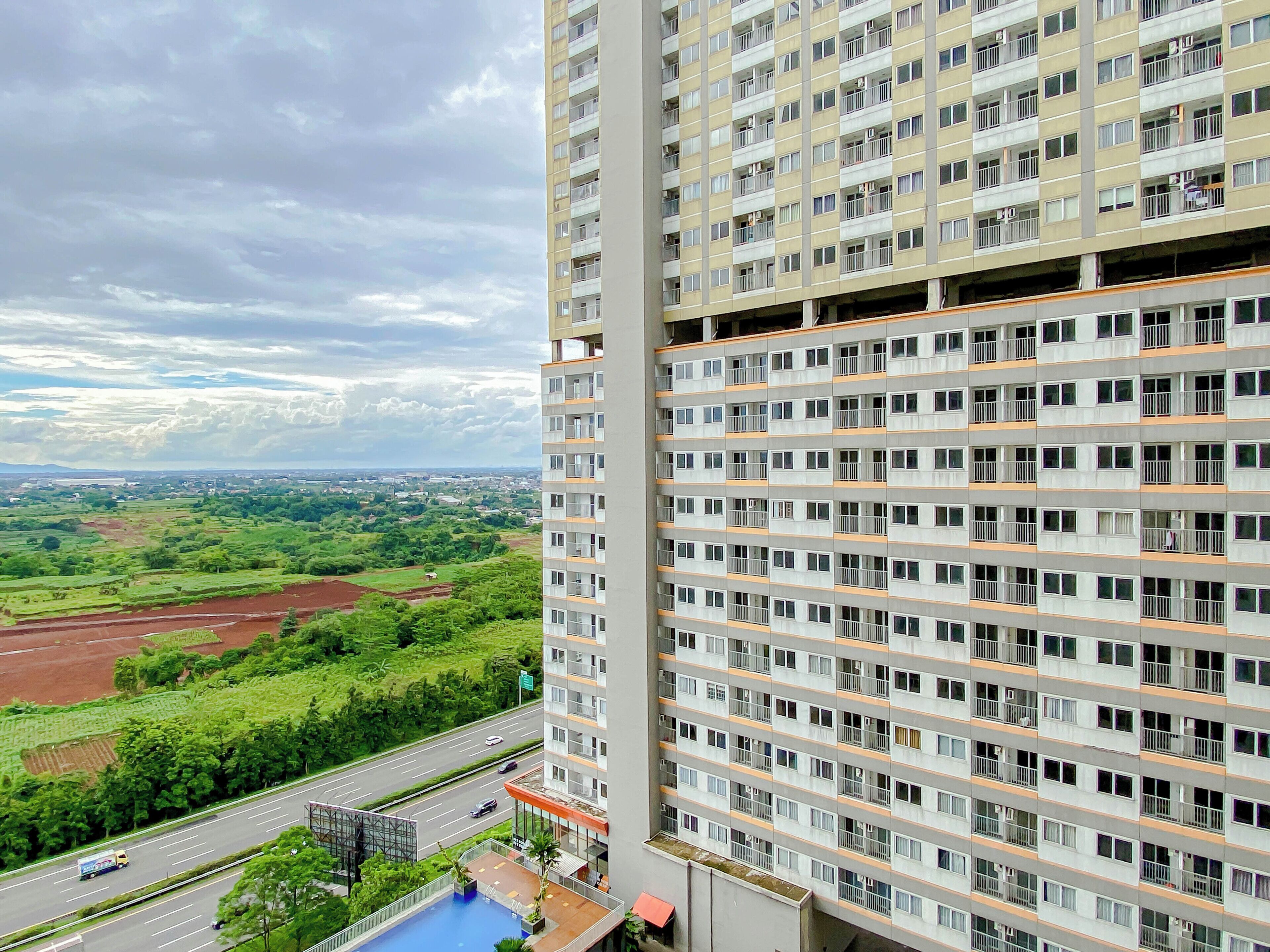 Un edificio de gran altura con varios balcones, una piscina y vistas a un paisaje verde.
