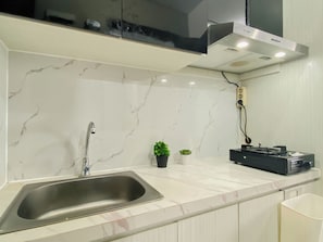 A kitchen with a stainless steel sink, a stove, a range hood, and a marble backsplash. - Minimalist And Airy Studio Apartment At Royal Sentul Park (Bogor)