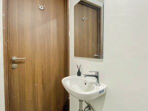 Eine Holztür mit Schlüsselloch und Griff, ein weißes Waschbecken mit Wasserhahn und ein Spiegel darüber.
