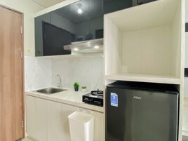 A kitchen with a stainless steel sink, a black refrigerator, and a marble countertop.