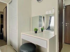 A room with a white desk, a black stool, a mirror, and a door.