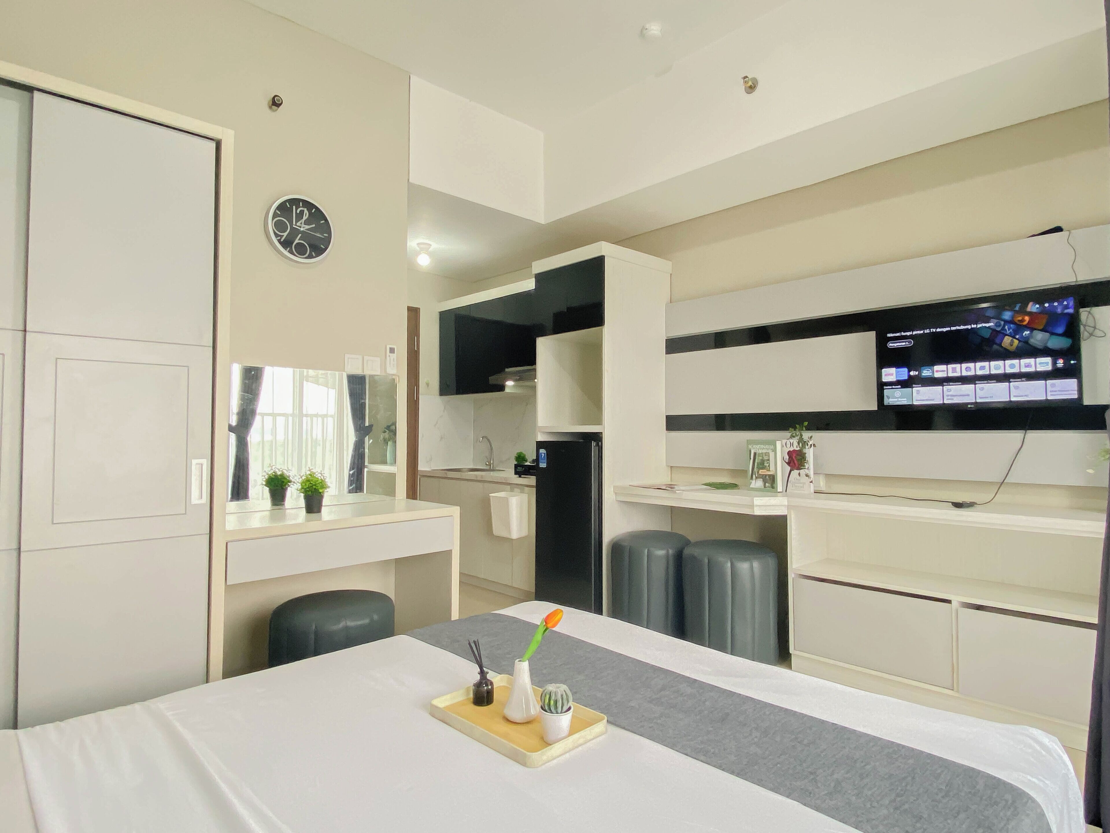 Ein modernes Hotelzimmer mit Bett, Schreibtisch, Fernseher, einer Uhr und einem Fenster.