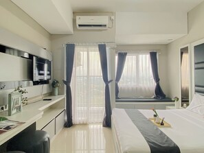 Ein Hotelzimmer mit einem Bett, einem Schreibtisch mit Computer, einem Fernseher und einem Fenster mit Vorhängen.