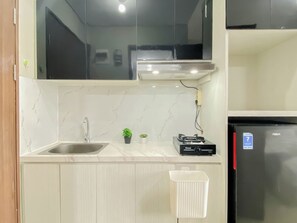 A kitchen with a stainless steel sink, a gas stove, a refrigerator, and a small potted plant. - Minimalist And Airy Studio Apartment At Royal Sentul Park (Bogor)