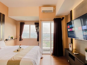 Ein Hotelzimmer mit Bett, Fernseher, einem Balkon mit Vorhängen und einer Klimaanlage.