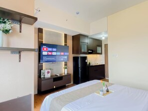 A hotel room with a bed, a TV mounted on the wall, a small kitchenette, and a shelf with decorative items. - Wooden Touch Studio Room At Apartment Lrt City Sentul - Royal Sentul Park (Bogor)