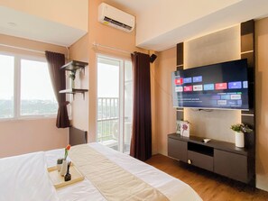 A hotel room with a bed, a TV displaying streaming services, a balcony with curtains, and a wall-mounted air conditioner. - Wooden Touch Studio Room At Apartment Lrt City Sentul - Royal Sentul Park (Bogor)