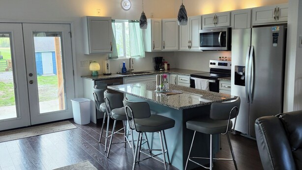 A modern kitchen with a central island, bar stools, stainless steel appliances, and a view through the sliding doors.