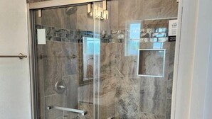 A glass-enclosed shower with a marble wall, a white toilet, and a visible shower control panel.