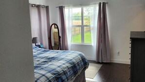 A bedroom with a bed, a ceiling fan, a window with curtains, a dresser, and a mirror.