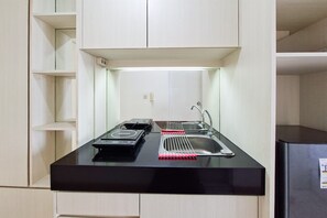 A compact kitchen with a black countertop, a gas stove, a sink, and a stainless steel refrigerator. - Serene Studio At Apartment M-Town Residence (Gading Serpong)