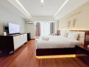 Ein Hotelzimmer mit Bett, Schreibtisch mit Computer, Fernseher und einem Fenster mit Vorhängen.