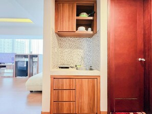 A compact kitchenette with a microwave, sink, and wooden cabinets. - Best Deal Studio At Mataram City Apartment (Ngaglik)