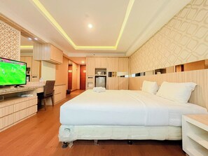 A hotel room with a bed, a TV, a desk, and a wardrobe. - Good Deal Studio Apartment At Mataram City (Yogyakarta)