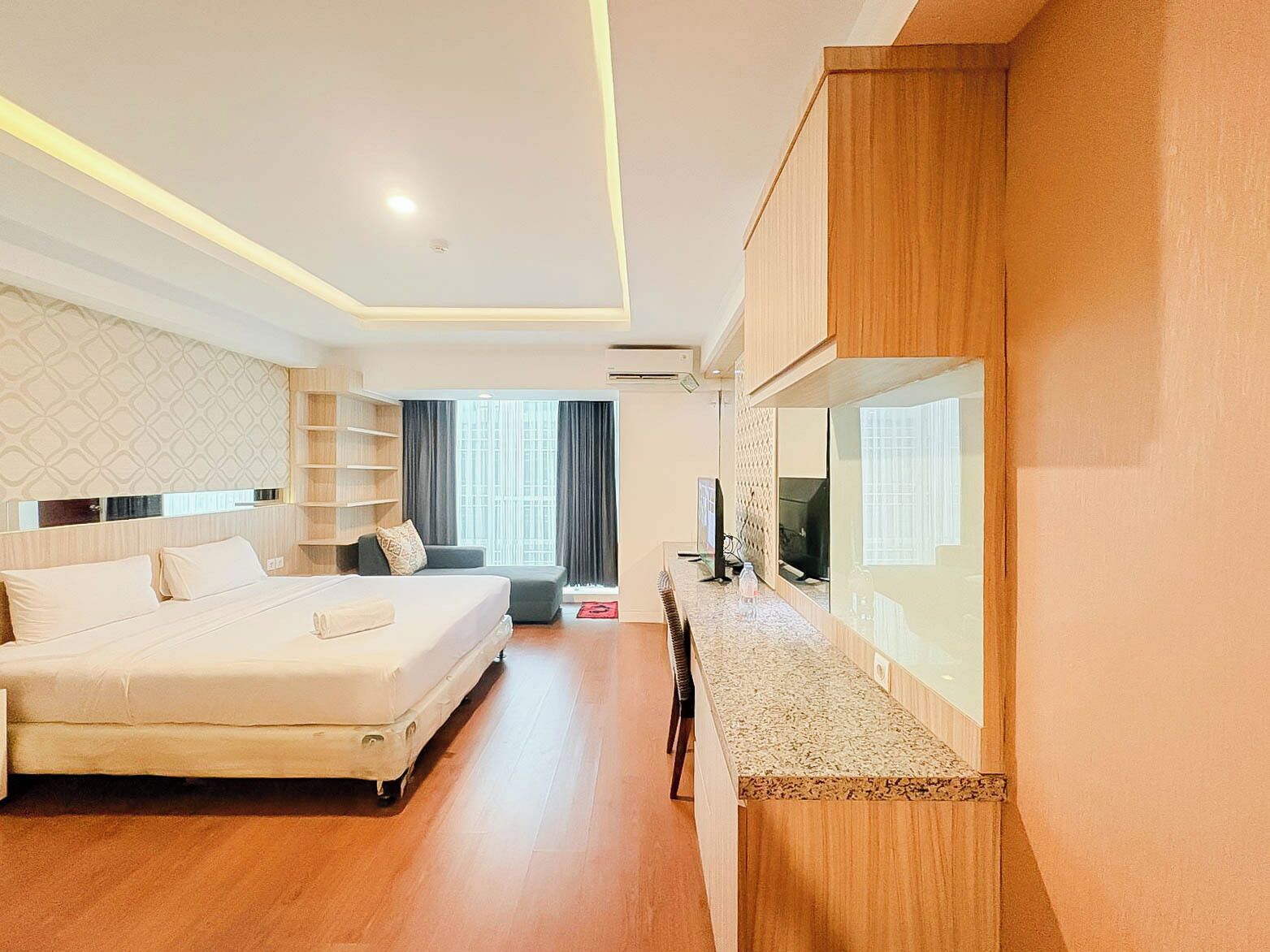 A modern hotel room with a bed, a TV, a desk, and a large window.