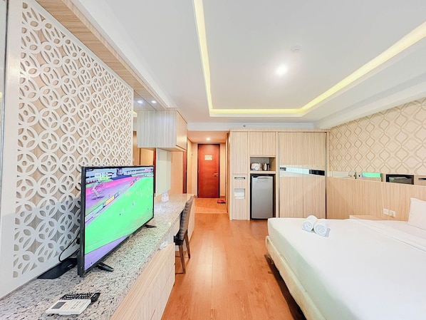 Habitación de hotel con televisión, cama, kitchenette y un detalle decorativo en la pared.