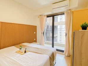 Una camera d'hotel con un letto, una testiera in legno, una finestra con tende, un balcone e un condizionatore d'aria.