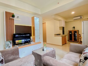 A living room with a flat-screen TV, a small table with a vase, and two sofas. - Neat Beige 2Br At Apartment Meikarta District 1 Near Dian Harapan School (Cikarang)