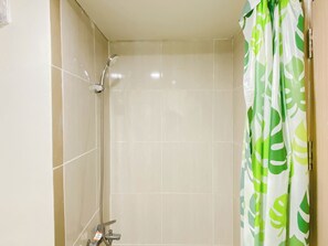 Doccia con soffione a mano, rubinetto a muro e tenda da doccia con motivo a foglia verde.