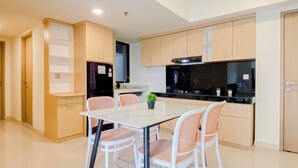 A modern kitchen with a dining area, featuring light wood cabinets, a black refrigerator, and a white dining table with chairs. - 5 Pax Convenient And Homey 3Br At Meikarta Apartment (Cikarang)