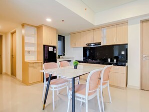 A modern kitchen with a dining area, featuring light wood cabinets, a black refrigerator, and a white dining table with chairs.