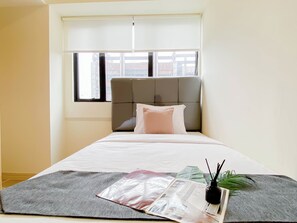 A hotel room with a bed, a window, and a plant on the bedside table. - 5 Pax Convenient And Homey 3Br At Meikarta Apartment (Cikarang)