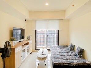 A living room with a sofa, a TV, a small table, and a window with blinds.