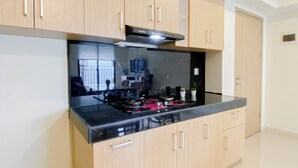 A modern kitchen with light wood cabinets, a black countertop, and a stainless steel range hood. - 5 Pax Convenient And Homey 3Br At Meikarta Apartment (Cikarang)
