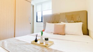 A hotel room with a bed, a bedside table with a tray, a vase, and a potted plant. - 5 Pax Convenient And Homey 3Br At Meikarta Apartment (Cikarang)