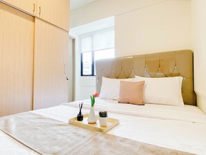 Una habitación de hotel con una cama, una mesita de noche con una bandeja, un florero y una planta en maceta.