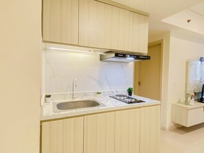 A modern kitchen with a built-in stove, sink, and a stainless steel range hood. - Cozy 3Br Apartment With Minimalist Style At Meikarta (Cikarang)