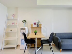 Ein modernes Zimmer mit einem Holztisch, zwei schwarzen Stühlen, einem grauen Sofa und einer weißen Regaleinheit mit Dekorationselementen.