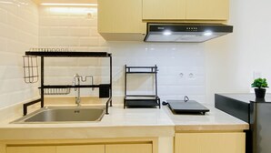 A kitchen with a sink, a black Rinnai dishwasher, wooden cabinets, and a potted plant on the countertop. - Restful And Spacious 3Br At Apartment Meikarta District 1 (Cikarang)