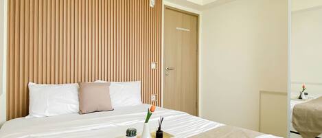 A hotel room with a bed, a wooden headboard, an air conditioning unit, a door, and a small table with a plant and a tray.