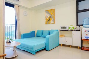 Ein Zimmer mit einem blauen Sofa, einem weißen Schrank, einem Wasserspender und einem Bild an der Wand.