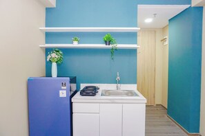 Eine kleine Küche mit einem blauen Kühlschrank, weißen Schränken, einer Spüle und Blumentöpfen auf Regalen.
