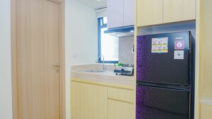 A kitchen with a refrigerator, a sink, and wooden cabinets. - 2Br Near Paramadina University At Meikarta District 2 Apartment (Cikarang)