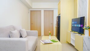 A modern living room with a sofa, a coffee table with a magazine, a TV, and a cabinet. - 2Br Near Paramadina University At Meikarta District 2 Apartment (Cikarang)
