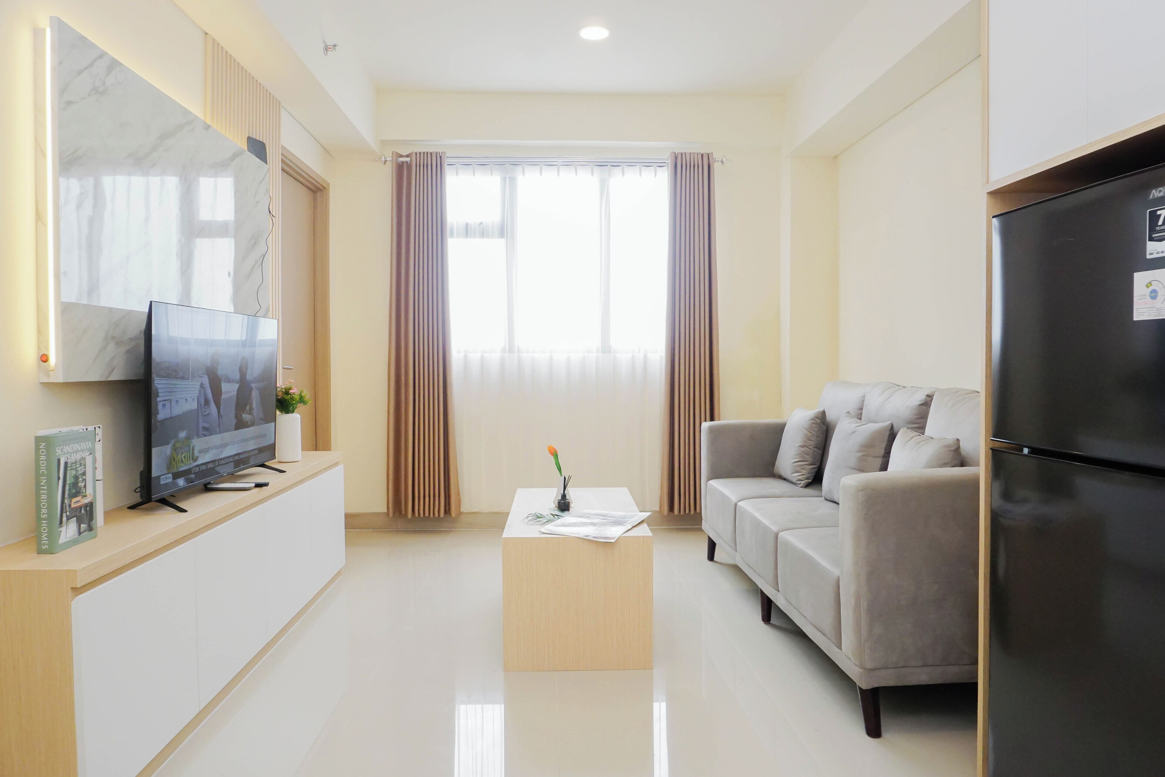 Uma sala de estar moderna com televisão de tela plana, um sofá, uma mesa de centro e uma geladeira.