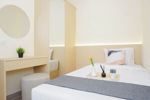 Ein modernes Hotelzimmer mit Bett, Nachttisch, einem kleinen Hocker, einem Spiegel und einem Nachttisch mit Vase, Kerze und Pflanze.